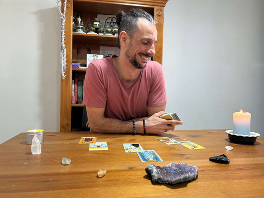 Man sitting at a table with tarot cards and crystals, smiling.