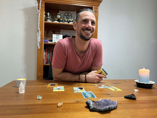 Man sitting at a table with tarot cards and crystals, smiling.