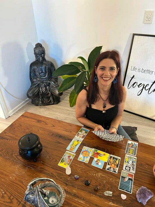 Woman performing a Tarot reading with cards on a table, surrounded by crystals and a statue.